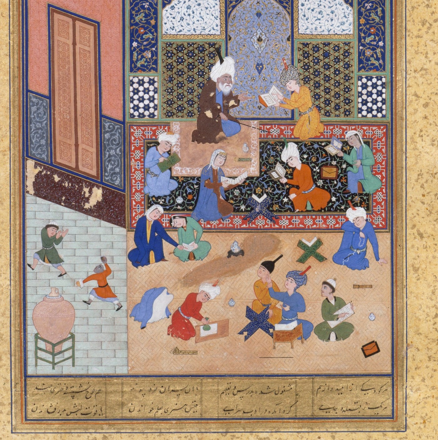 A manuscript painting of a school. A bearded master in a white turban sits in a tiled niche beside a pupil holding an open book, while other pupils read, write on tablets, and work at folding bookstands on the carpet and in the courtyard below